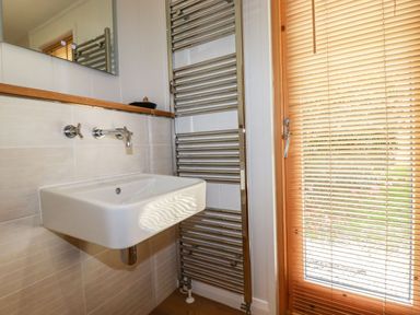 A bathroom sink with wall-mounted taps and a chrome towel radiator next to a window with wooden blinds at 4 Water's Edge in Lanreath