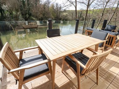 Outdoor wooden table with four chairs on a deck overlooking a body of water with trees at 4 Waters Edge in Lanreath
