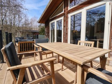 An outdoor wooden deck with a table and chairs next to glass doors at 4 Water's Edge in Lanreath