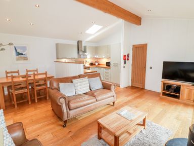 An open living room with leather sofas a wooden coffee table a dining table a kitchen area and a television at 6 Water's Edge Lanreath