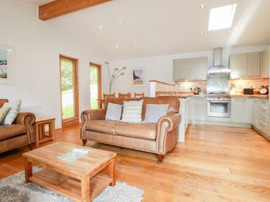 An open-plan living room and kitchen with leather sofas wooden coffee table and dining table at 6 Water's Edge in Lanreath