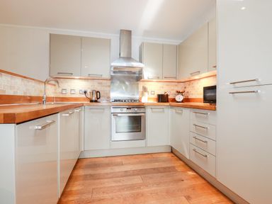 A kitchen with wooden floors beige cabinets a stainless steel oven stove and range hood at 6 Water's Edge in Lanreath