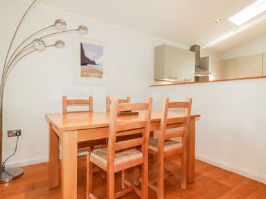 A dining area with a wooden table and four chairs next to a kitchen with cabinets and a cooker hood at 6 Water's Edge in Lanreath