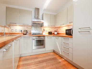 A kitchen with wooden countertops white cabinets a stainless steel oven and stove a kettle a microwave and a knife block at 6 Water's Edge Lanreath