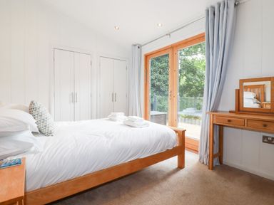 A bedroom with a wooden bed a dressing table white wardrobes and glass doors at 6 Water's Edge in Lanreath