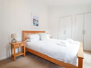 A bedroom with a wooden bed frame and two wooden bedside tables with lamps at 6 Waters Edge in Lanreath