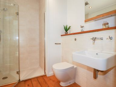 A bathroom with a glass-enclosed shower a toilet and a wall-mounted sink at 6 Water's Edge in Lanreath