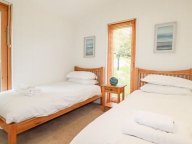 A bedroom with two single beds wooden frames white bedding a small wooden nightstand and two framed pictures at 6 Water's Edge in Lanreath