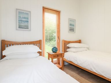 A bedroom with two single beds a small wooden table and a window with blinds at 6 Water's Edge in Lanreath