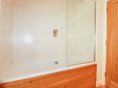 A bathroom with a bathtub featuring a wooden panel and a glass shower screen at 6 Water's Edge in Lanreath
