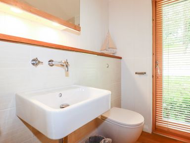 A bathroom with a white sink and toilet next to a window with wooden blinds at 6 Water's Edge Lanreath