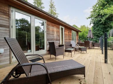 An outdoor wooden deck with brown wicker furniture and glass doors at 6 Water's Edge in Lanreath