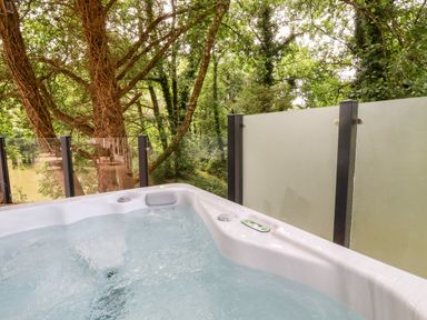 An outdoor hot tub next to glass and frosted panels with trees in the background at 6 Waters Edge in Lanreath