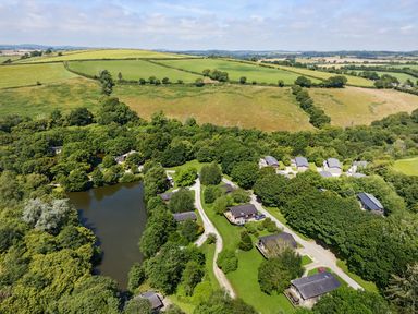 An aerial view of cottages around a pond and surrounded by trees and fields at 6 Water's Edge in Lanreath