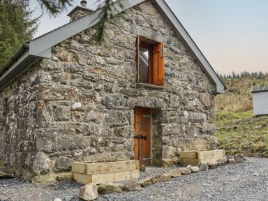 A small stone building with a wooden door and an open wooden window with planters outside at Brithgwm Canol in Brithdir near Dolgellau