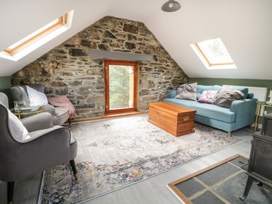 A living room with a stone wall a wooden window two skylights two armchairs a sofa a wooden chest and a rug at Brithgwm Canol in Brithdir near Dolgellau