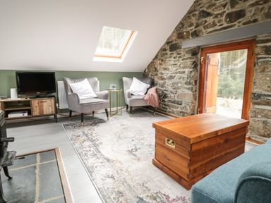 A sitting area with two armchairs a wooden chest a TV on a stand and a stone wall at Brithgwm Canol in Brithdir near Dolgellau