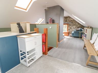 An attic room with a white kitchen cart, wooden bench with pillows, a blue sofa, bookshelves, and stone wall at Brithgwm Canol Brithdir near Dolgellau