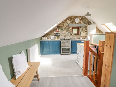 A kitchen with blue cabinets stone wall and wooden bench with white pillows at Brithgwm Canol in Brithdir near Dolgellau