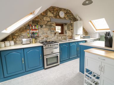 A kitchen with blue cabinets a stone wall a gas oven a toaster and utensils at Brithgwm Canol in Brithdir near Dolgellau