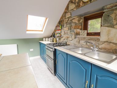 A kitchen with blue cabinets a double sink a stove and a stone wall at Brithgwm Canol in Brithdir near Dolgellau