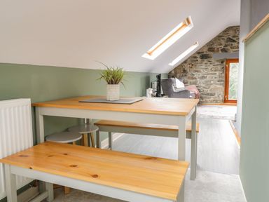 A dining area with wooden benches and table and a living space with armchair and stone wall at Brithgwm Canol in Brithdir near Dolgellau