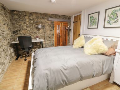 A bedroom with a bed with two pillows a desk and chair against a stone wall at Brithgwm Canol in Brithdir near Dolgellau