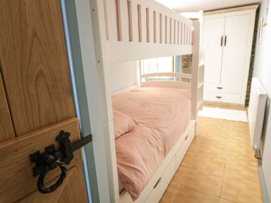 A bedroom with a white bunk bed pink bedding a wooden door and a white wardrobe at Brithgwm Canol in Brithdir near Dolgellau