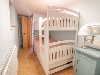 A small bedroom with white bunk beds a wooden door a radiator and a green cabinet with a lamp at Brithgwm Canol Brithdir near Dolgellau