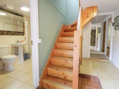 A hallway with wooden stairs next to a bathroom with a toilet and sink at Brithgwm Canol in Brithdir near Dolgellau