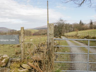 A metal gate and wooden fence posts at the entrance to a rural gravel road with fields and sheep at Brithgwm Canol in Brithdir near Dolgellau