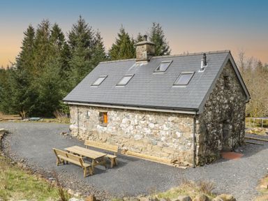 A stone house with a slate roof and skylights surrounded by trees and outdoor wooden picnic benches at Brithgwm Canol in Brithdir near Dolgellau