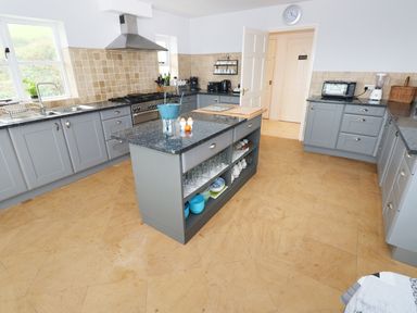 A kitchen with gray cabinets an island with dishes and glasses and appliances on countertops at The Sandcastle in Freshwater East