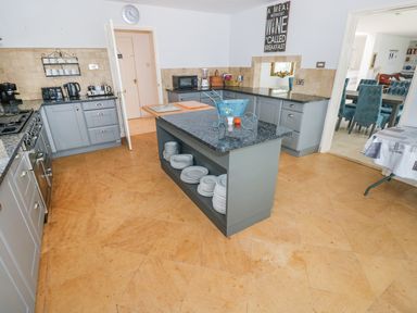 A kitchen with gray cabinets a central island with plates and a dining room visible through the doorway at The Sandcastle in Freshwater East