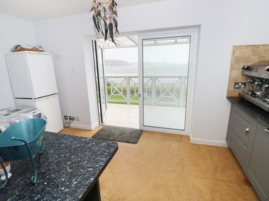 A kitchen with a refrigerator countertop and coffee machine near a sliding glass door opening to a balcony with a sea view at The Sandcastle in Freshwater East