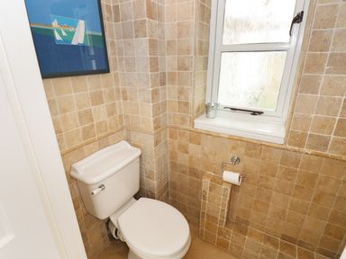A bathroom with a toilet next to a window and a framed picture on the tiled wall at The Sandcastle in Freshwater East