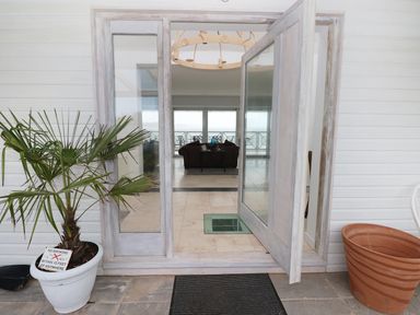 An open glass door leading to a room with a sofa and balcony with chairs and a table outside