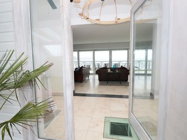 A tiled entrance leading to a living area with brown sofas and a glass door overlooking an outdoor patio at The Sandcastle in Freshwater East