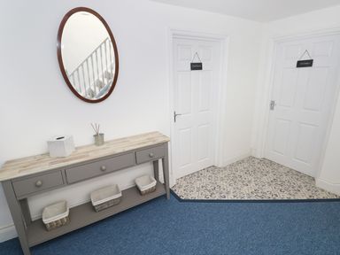 A hallway with a gray console table with baskets under it and an oval mirror above at The Sandcastle in Freshwater East
