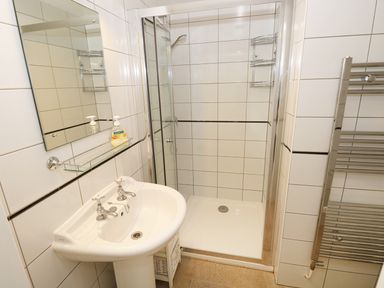A bathroom with a sink mirror shower area and a towel radiator at The Sandcastle in Freshwater East