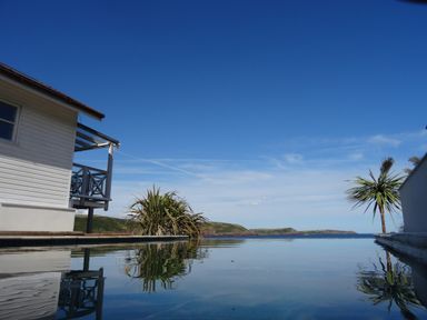 An outdoor pool with a house on the left and plants near the pool overlooking hills and ocean at The Sandcastle in Freshwater East