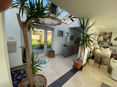 An indoor area with potted plants large glass doors leading outside a staircase a bookshelf and a sitting area with a lamp and couch at The Sandcastle in Freshwater East
