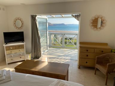 A bedroom with wooden furniture and a television overlooking a balcony with an ocean view at The Sandcastle in Freshwater East