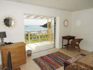 A room with a wicker dresser lamp colorful rug wooden desk wicker chair open doors to balcony overlooking sea at The Sandcastle in Freshwater East
