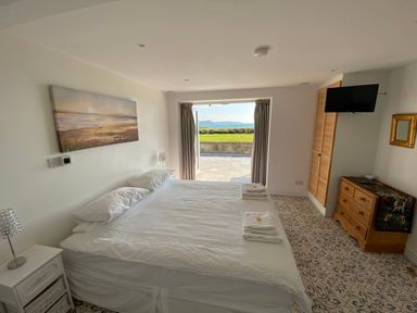 A bedroom with a double bed towels on the bed a chest of drawers and a TV on the wall at The Sandcastle in Freshwater East