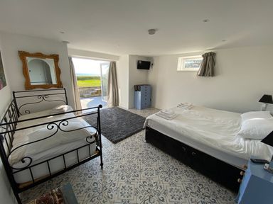 A bedroom with two beds a mirror a dresser a rug and an open door leading outside at The Sandcastle in Freshwater East