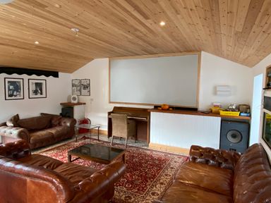 A living room with leather sofas, a piano, a glass coffee table, a red patterned rug, and framed pictures on the wall at The Sandcastle in Freshwater East