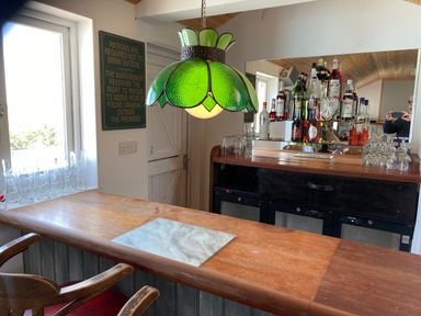An indoor bar area with a wooden counter green hanging lamp bottles of alcohol and glassware at The Sandcastle in Freshwater East