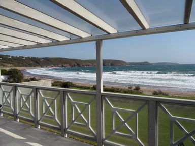 A covered balcony overlooking a beach and ocean with hills in the background at The Sandcastle in Freshwater East