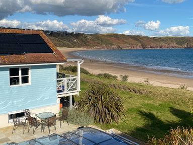 A blue beach house with outdoor chairs and table near a sandy beach and ocean at The Sandcastle in Freshwater East